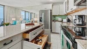 Una cocina moderna con armarios blancos, un refrigerador de acero inoxidable, una cafetera y vistas de la ciudad a través de amplios ventanales.