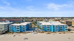 Un hotel frente a la playa con varios edificios azules, una playa de arena y cielo despejado.