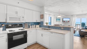 Una cocina moderna con armarios blancos, microondas, estufa y lavavajillas. Hay una ventana con vista al océano.