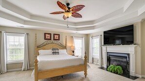 Un dormitorio con una cama grande, ventilador de techo, chimenea y televisor.