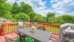 Una terraza con mesa y sillas, rodeada por una barandilla roja, con vistas a un paisaje verde exuberante.