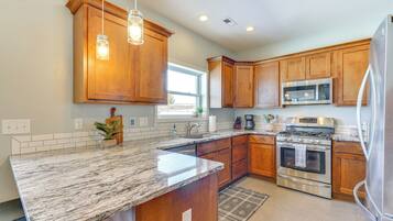 A kitchen with wooden cabinets, a granite countertop, stainless steel appliances, and pendant lighting.