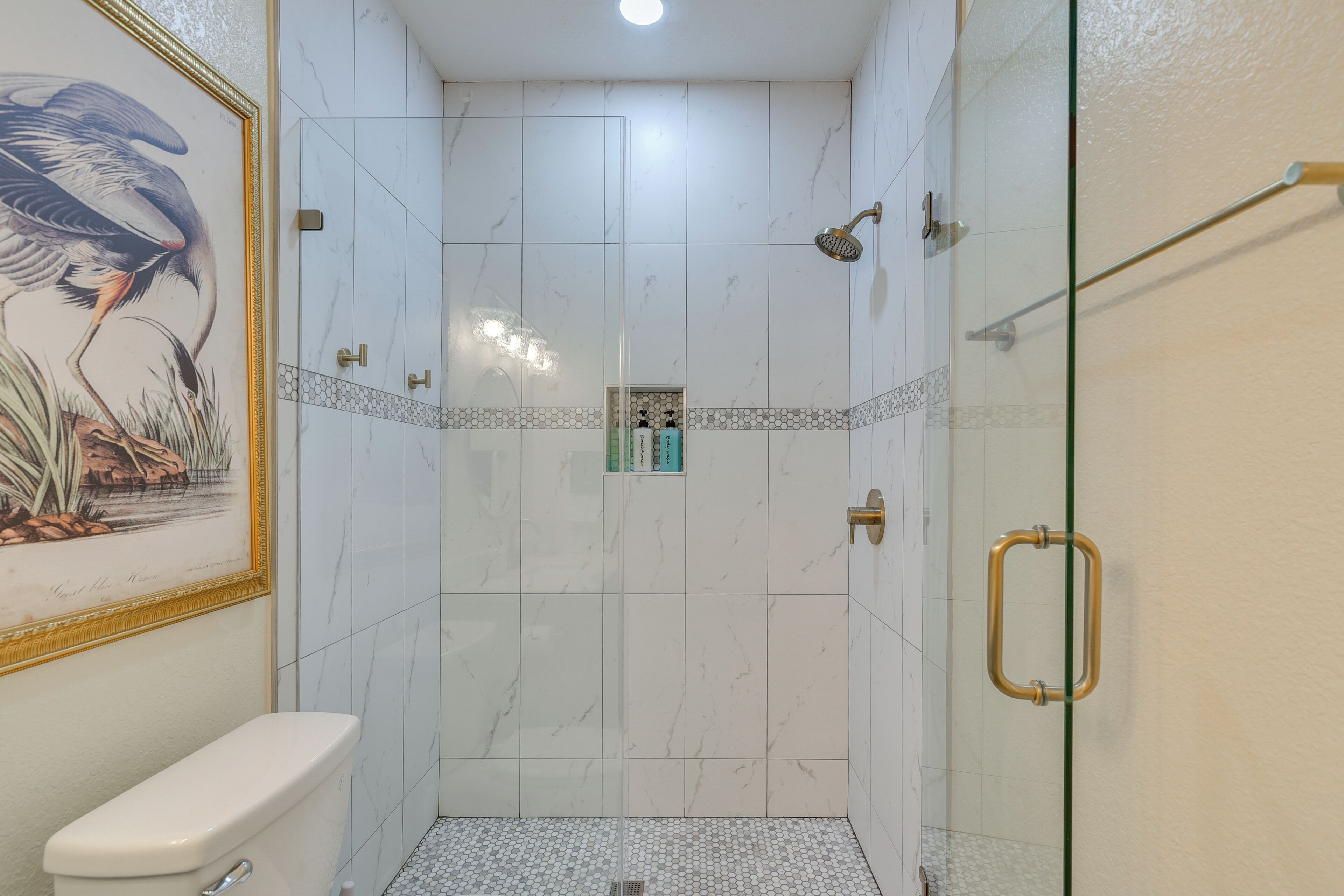 Et badeværelse med toilet, en bruseniche med glasdør og et billede i ramme på væggen.