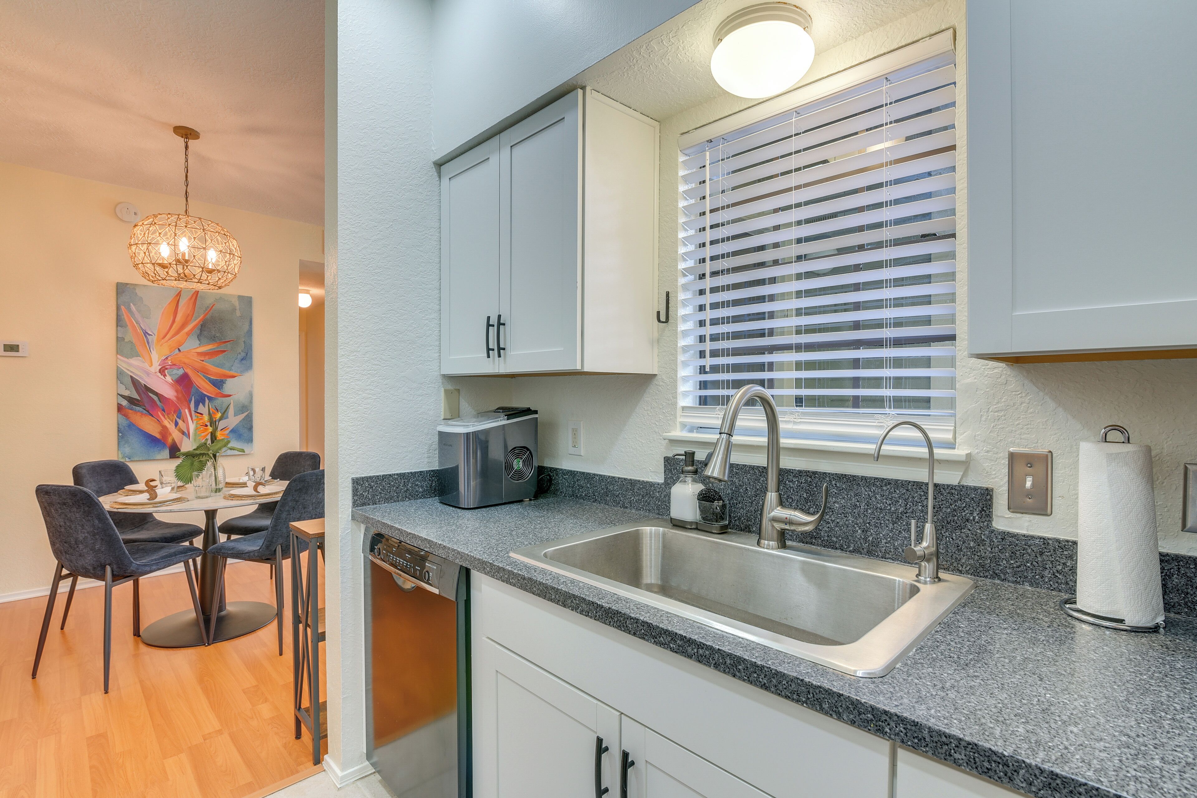 A modern kitchen with a granite countertop, stainless steel sink, and white cabinets.