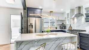 A modern kitchen with a marble island, stainless steel appliances, and gold bar stools. - 6 Mi to Spectrum Center: Spacious Getaway w/ Deck (Charlotte)
