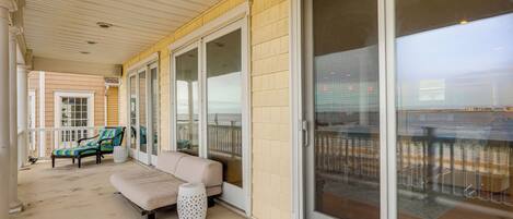 A covered porch with a beige couch, striped chairs, and a small table.