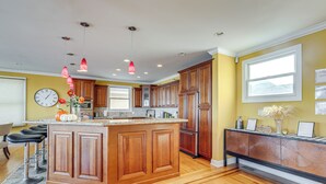 Una cocina con armarios de madera, una isla central, luces colgantes y un reloj en la pared.