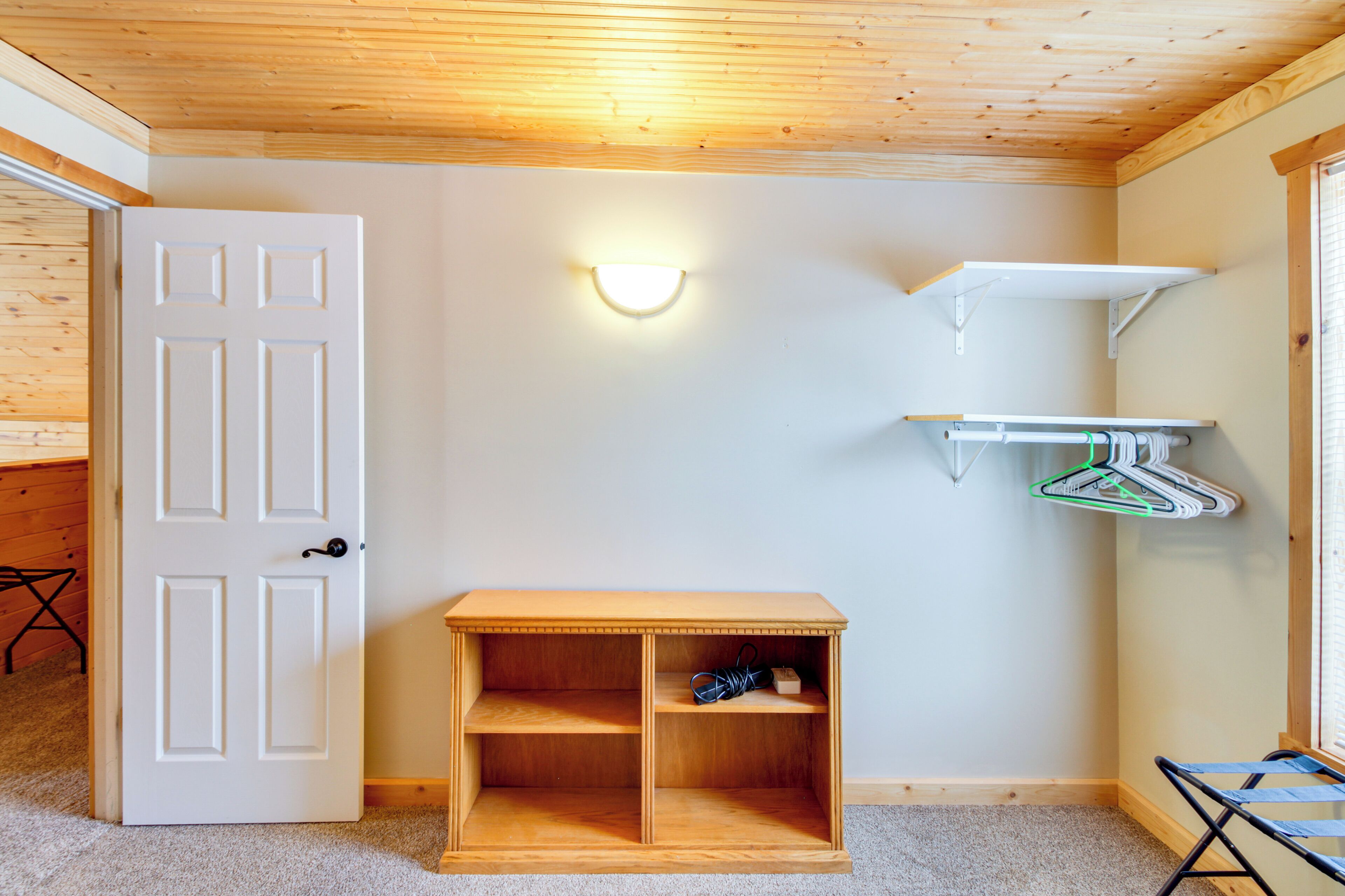 A room with a wooden door, a wall-mounted light fixture, a small wooden shelf, and a hanging clothes rack.
