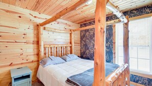 Une chambre dans un chalet en bois, avec un lit, une table de chevet et une fenêtre avec des stores.