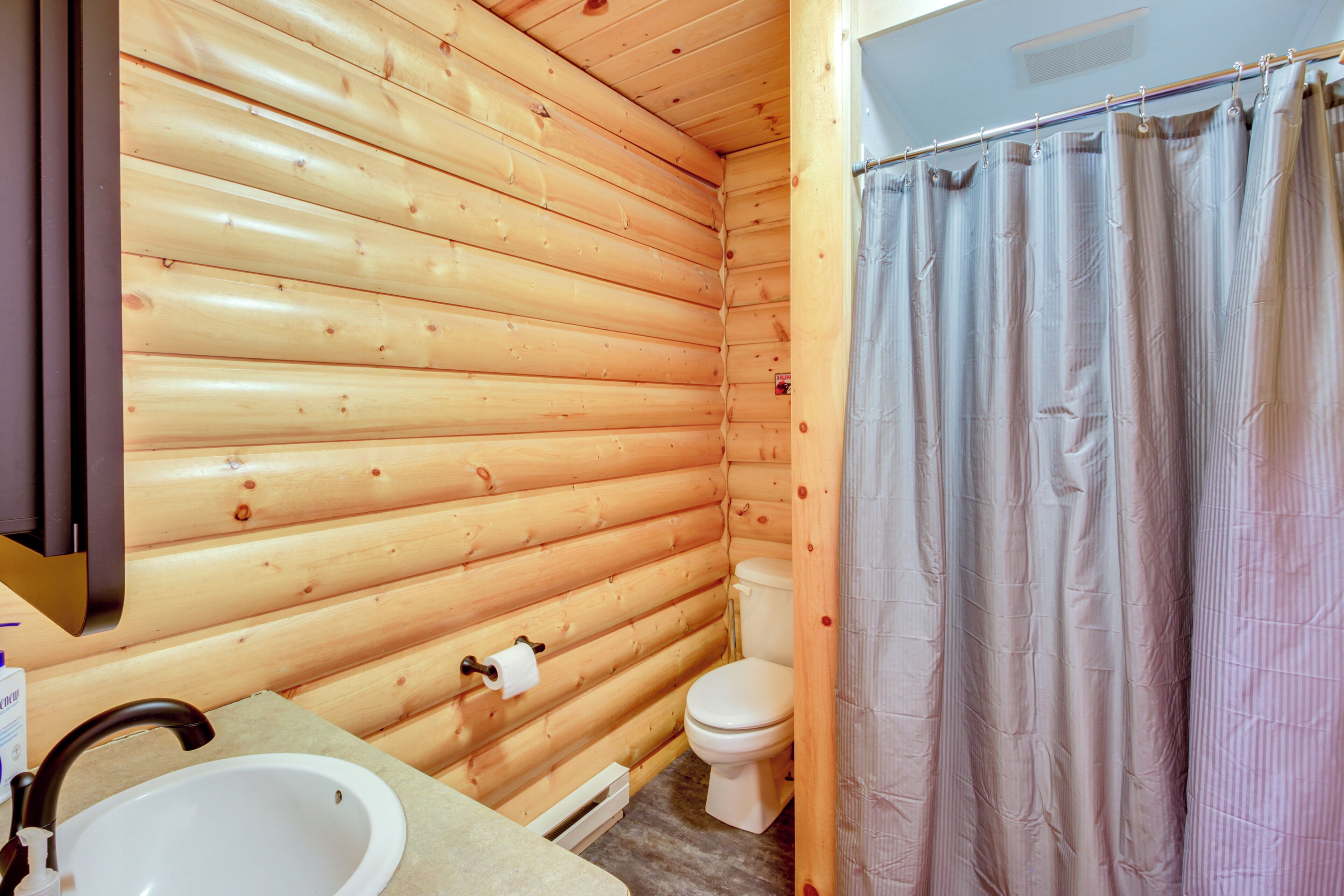 A wooden cabin bathroom with a sink, toilet, and shower curtain.