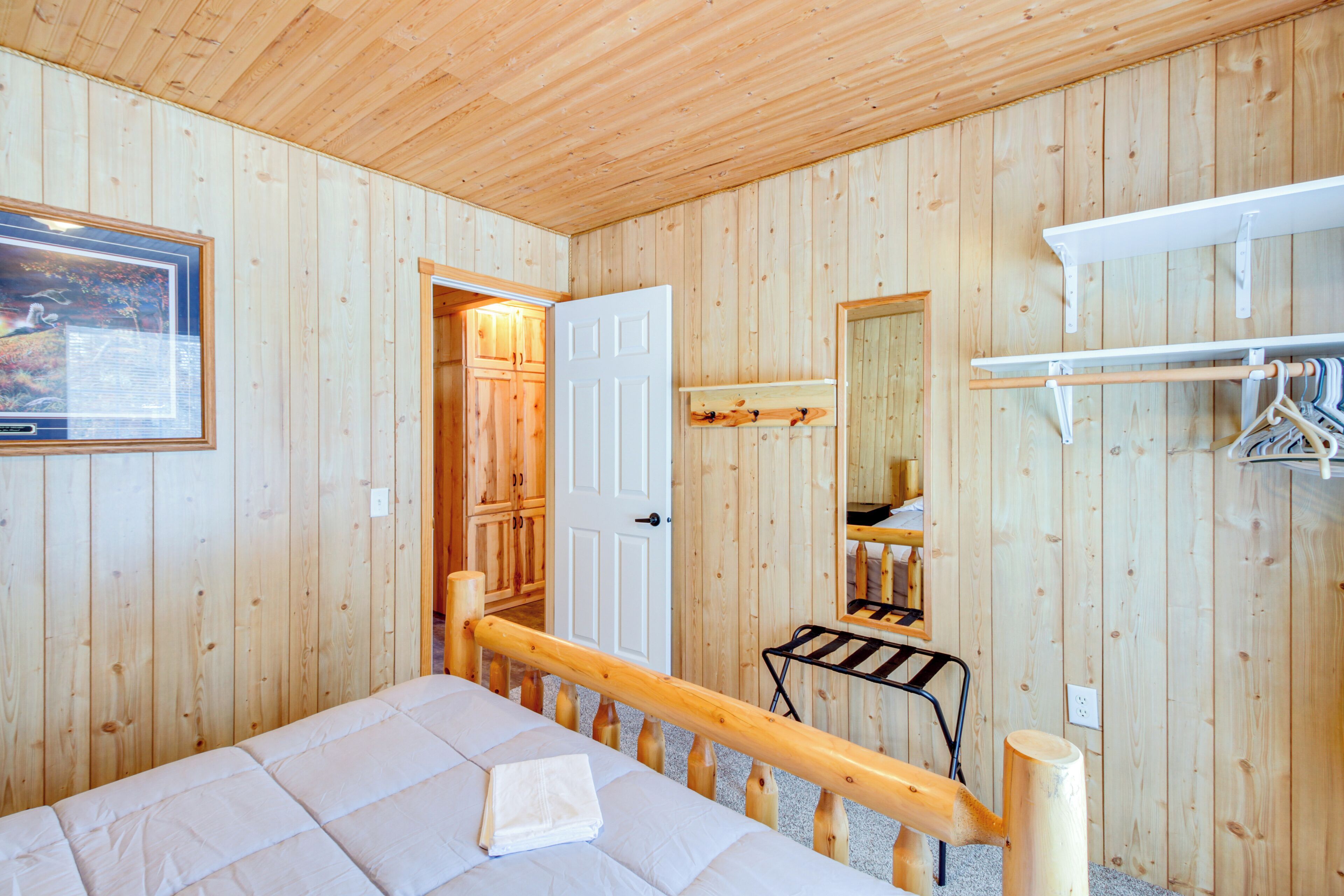 Een kamer met houten lambrisering, een bed, een deur naar een badkamer, een spiegel en een kapstok.