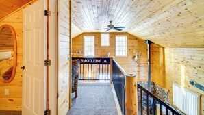 Un intérieur en bois avec un escalier, un ventilateur de plafond et une pancarte « Bienvenue ».