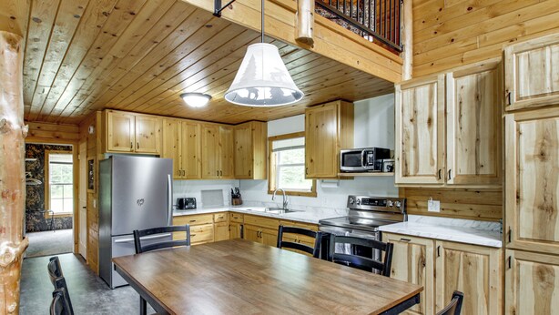 Une cuisine de style rustique, avec des murs en bois, une table à manger centrale, des meubles de rangement en bois et un luminaire suspendu.
