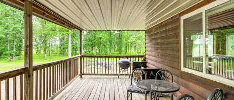 A wooden deck with a railing, a table with chairs, and a view of a forest.