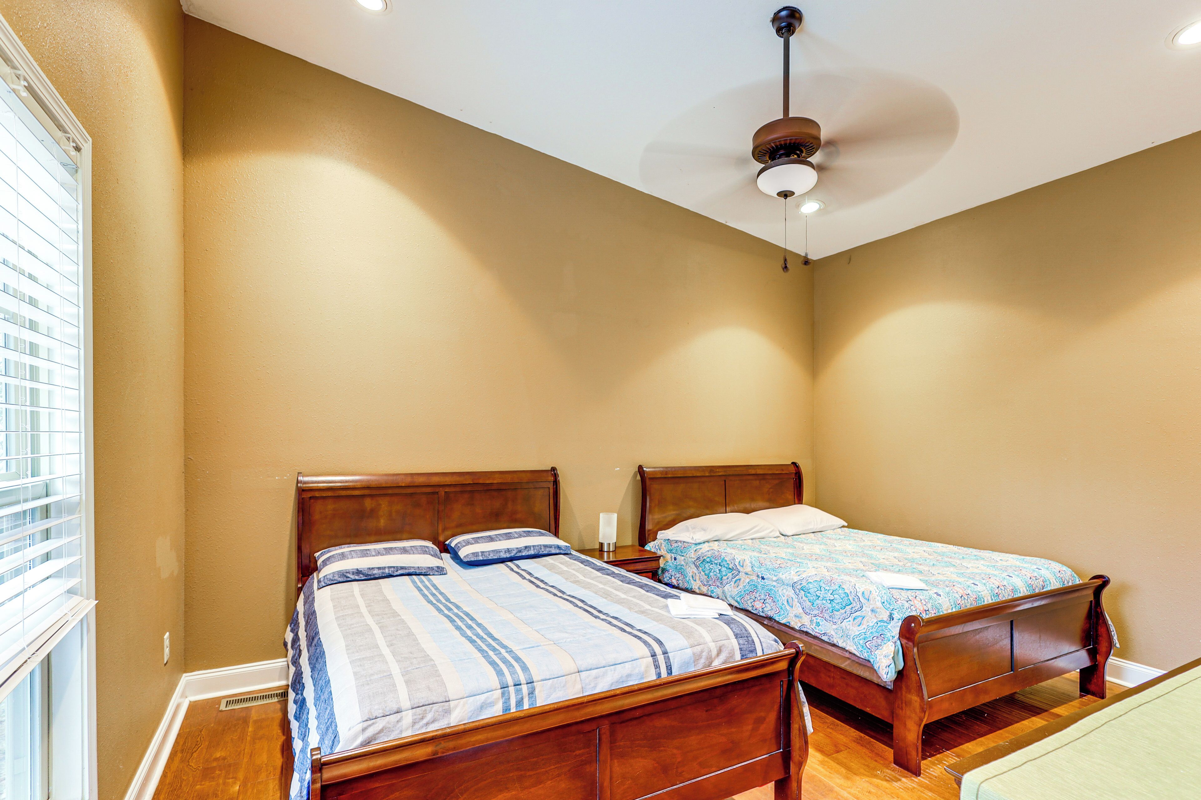 A bedroom with two wooden beds, a ceiling fan, and a window with blinds.