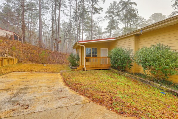 A single-story yellow house with a front porch, surrounded by a yard with grass and trees.