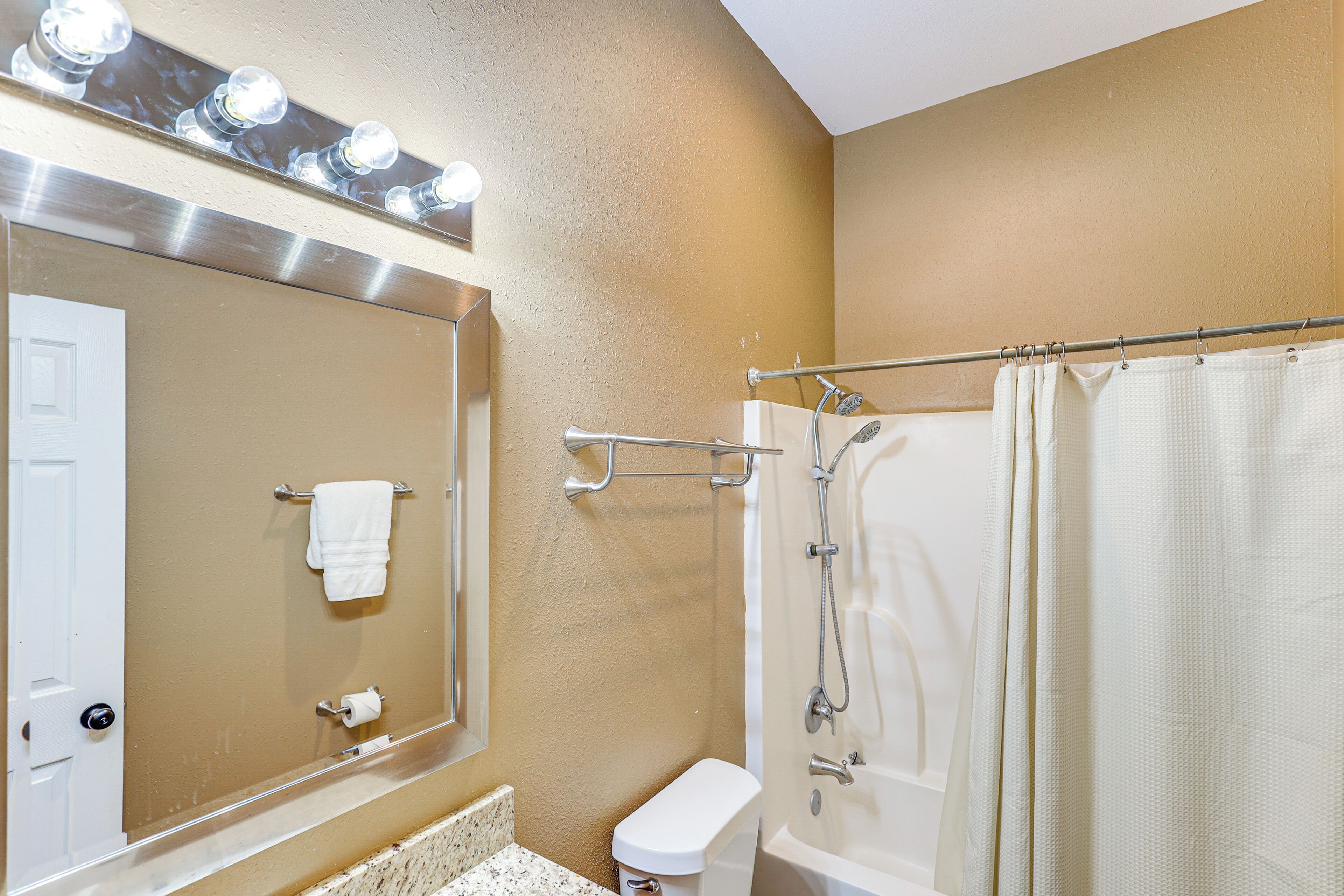 A bathroom with a toilet, a sink, a mirror with lights, and a shower with a curtain.