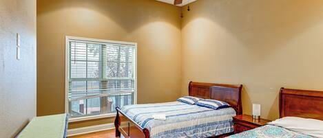 A bedroom with two wooden beds, a window with blinds, and a ceiling fan.