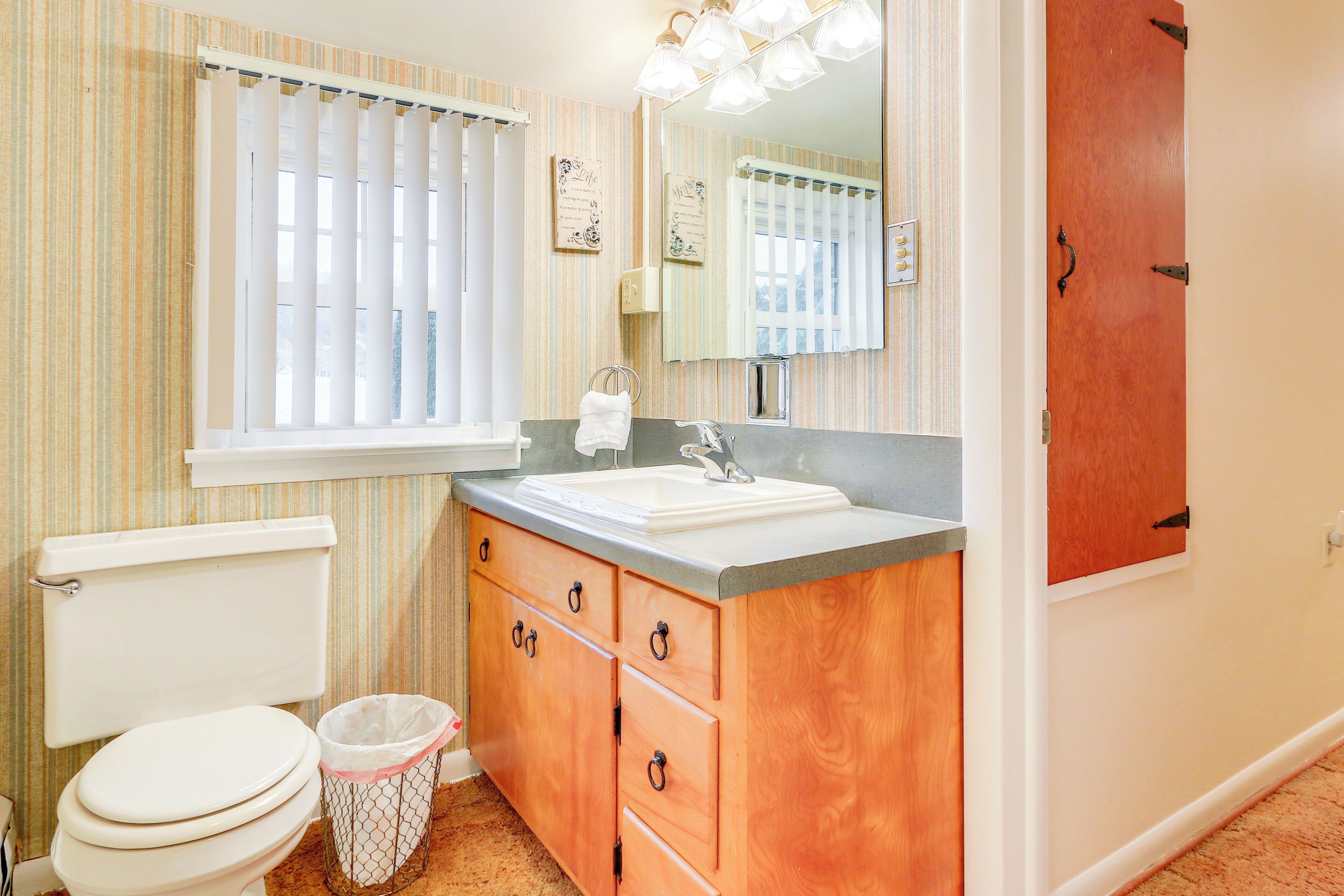 A bathroom with a toilet, sink, vanity, and a mirror.