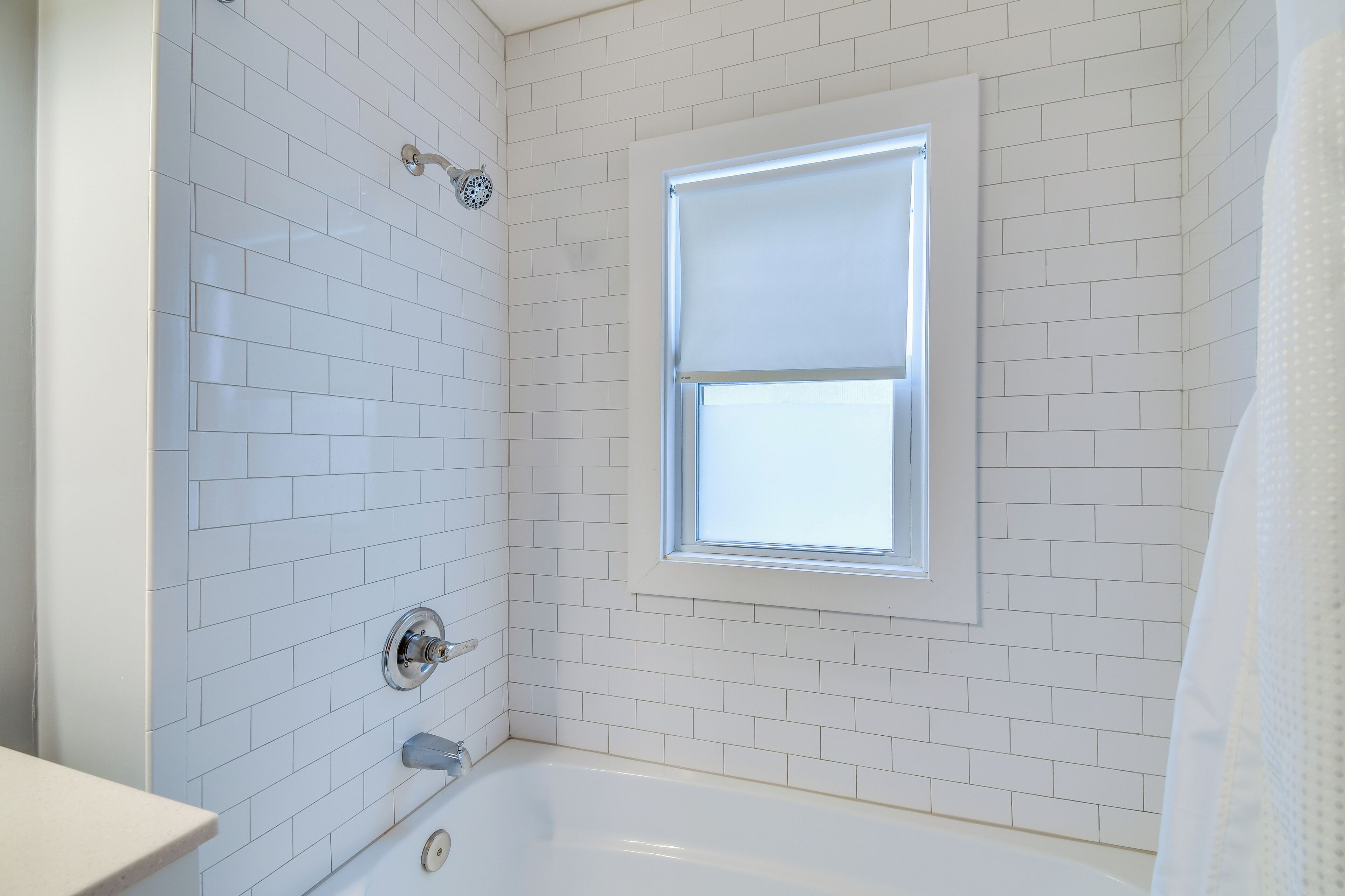 Een badkamer met witte betegelde wanden, een raam en een bad.