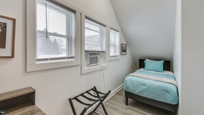 Een slaapkamer met een bed, een bureau en drie ramen.