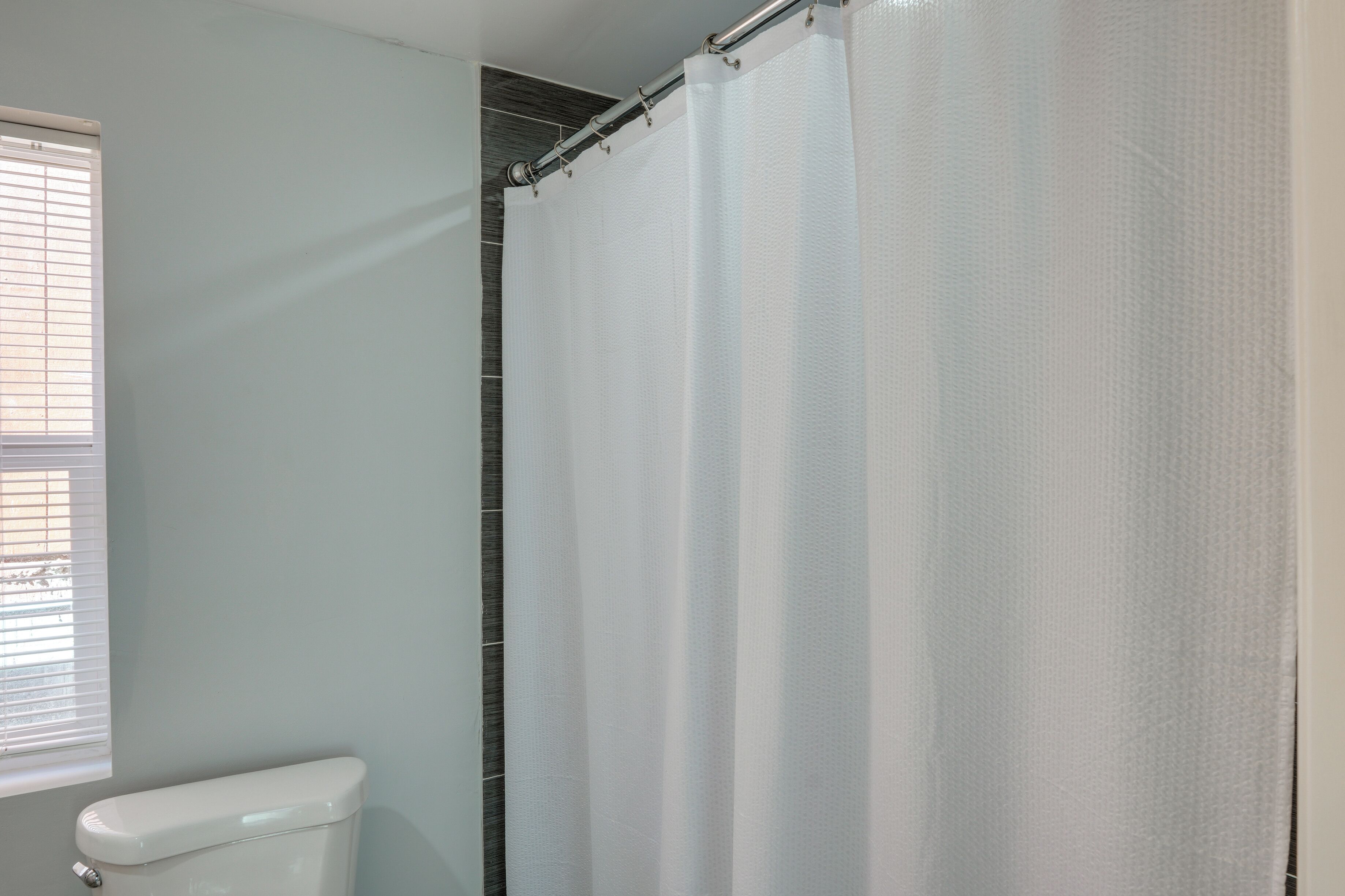 A bathroom with a toilet, a shower curtain, and a window with blinds.