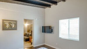A room with a patterned rug, a flat-screen TV mounted on the wall, and a window with blinds.