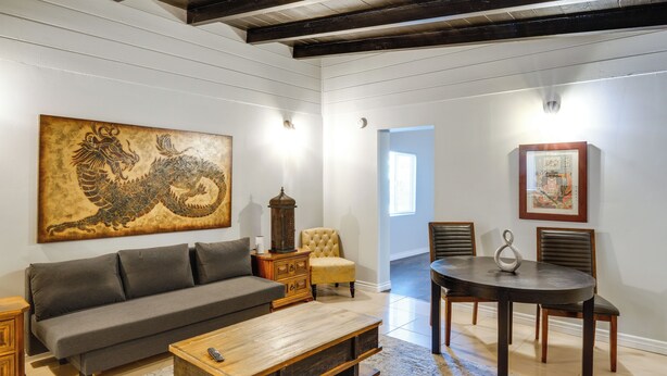 A living room with a sofa, coffee table, and a dining table with chairs. There is a large dragon painting on the wall and a small lantern on a side table.