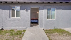 A building with a concrete exterior, a door leading to a room with a bed and a red pillow, and a small window on the right. - Mountain Views: Minimalist California Studio (Frazier Park)