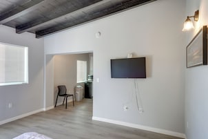 Una habitación con televisión de pantalla plana en la pared, techo con vigas a la vista y ventana con persianas.