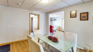 Comedor con mesa de vidrio, sillas blancas y un centro de mesa floral rojo.