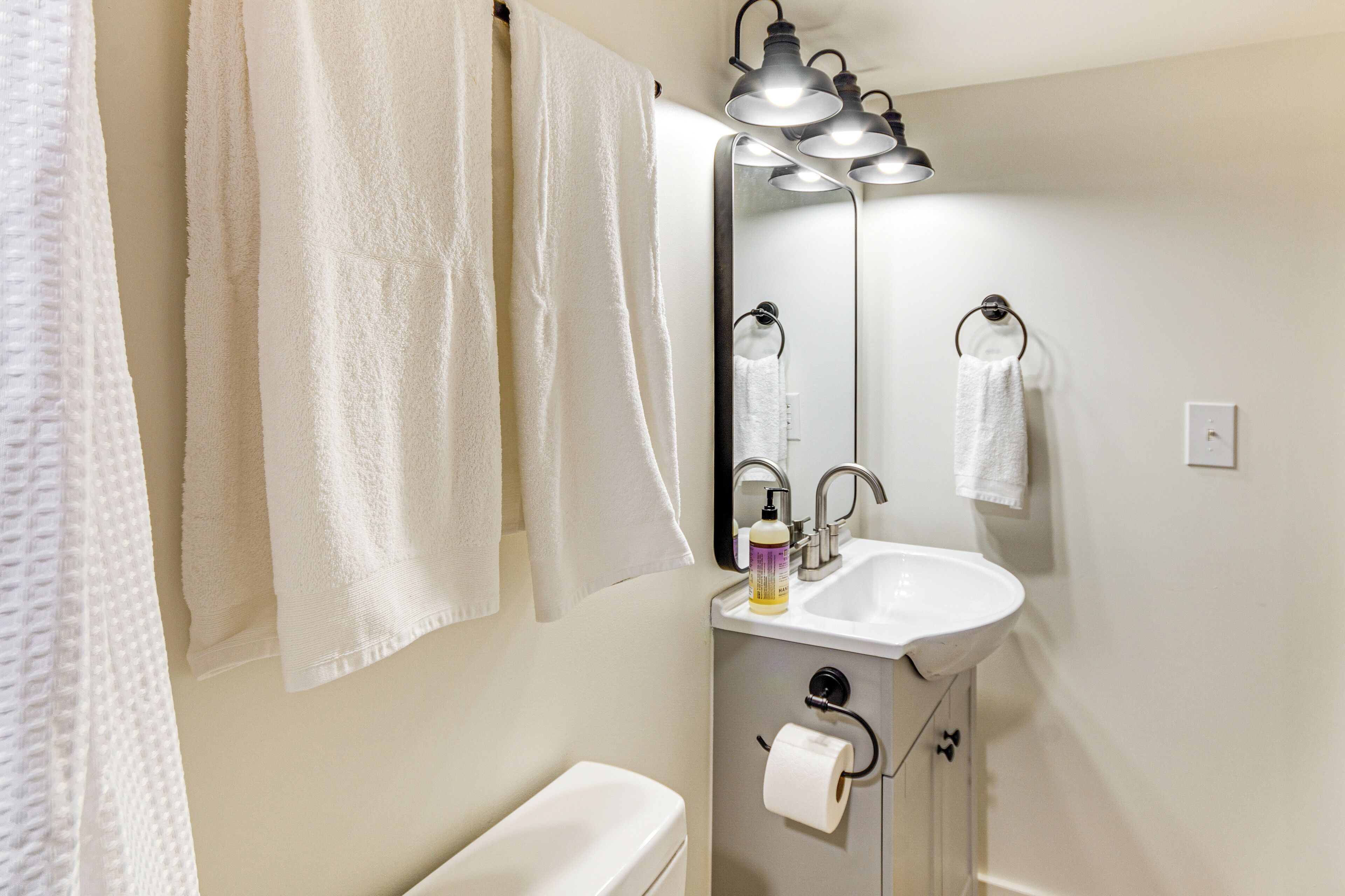 A bathroom with white towels hanging on the wall, a sink, a toilet, and a mirror with a light fixture above it.