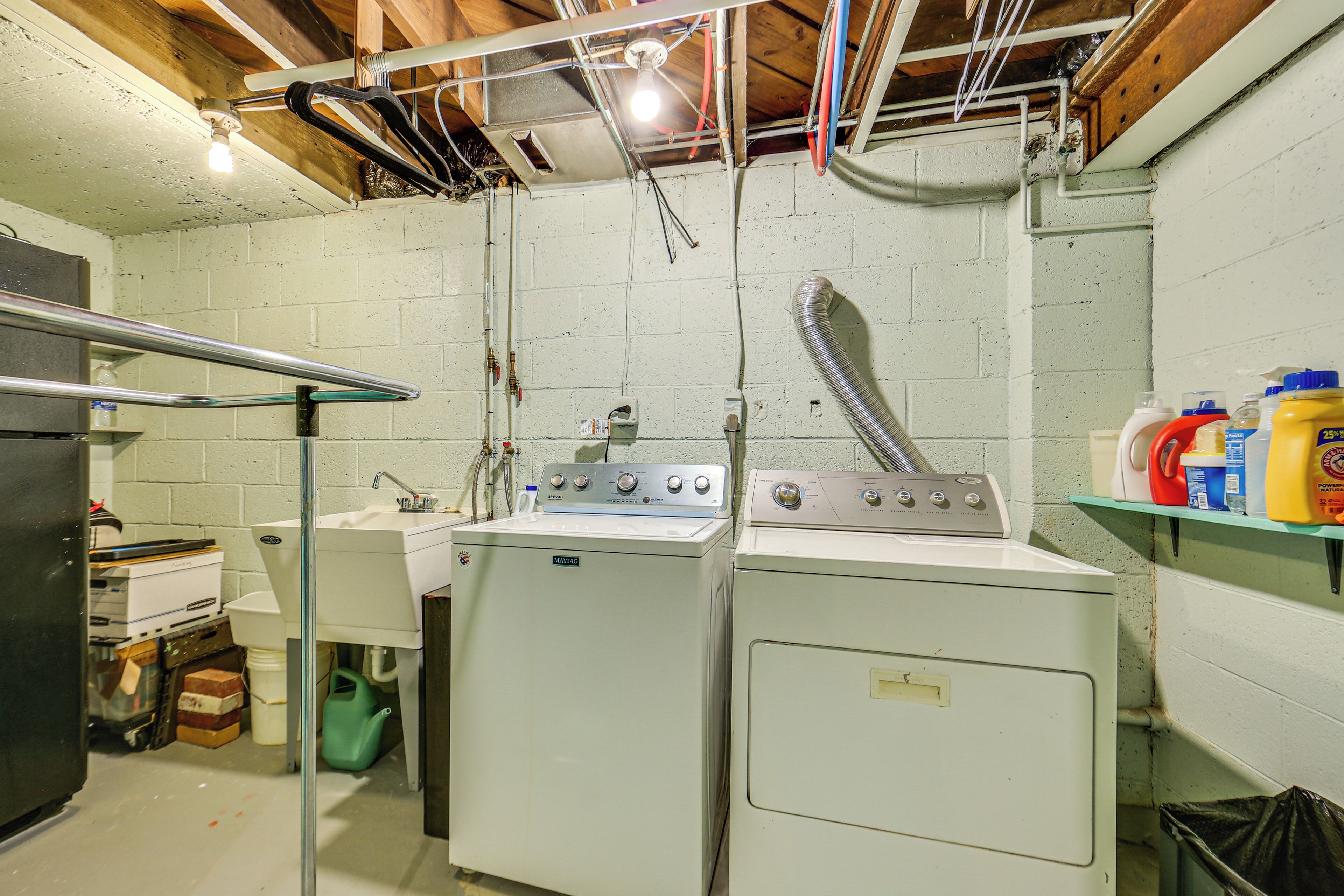 A laundry room with two washing machines, a sink, and a shelf with cleaning supplies.