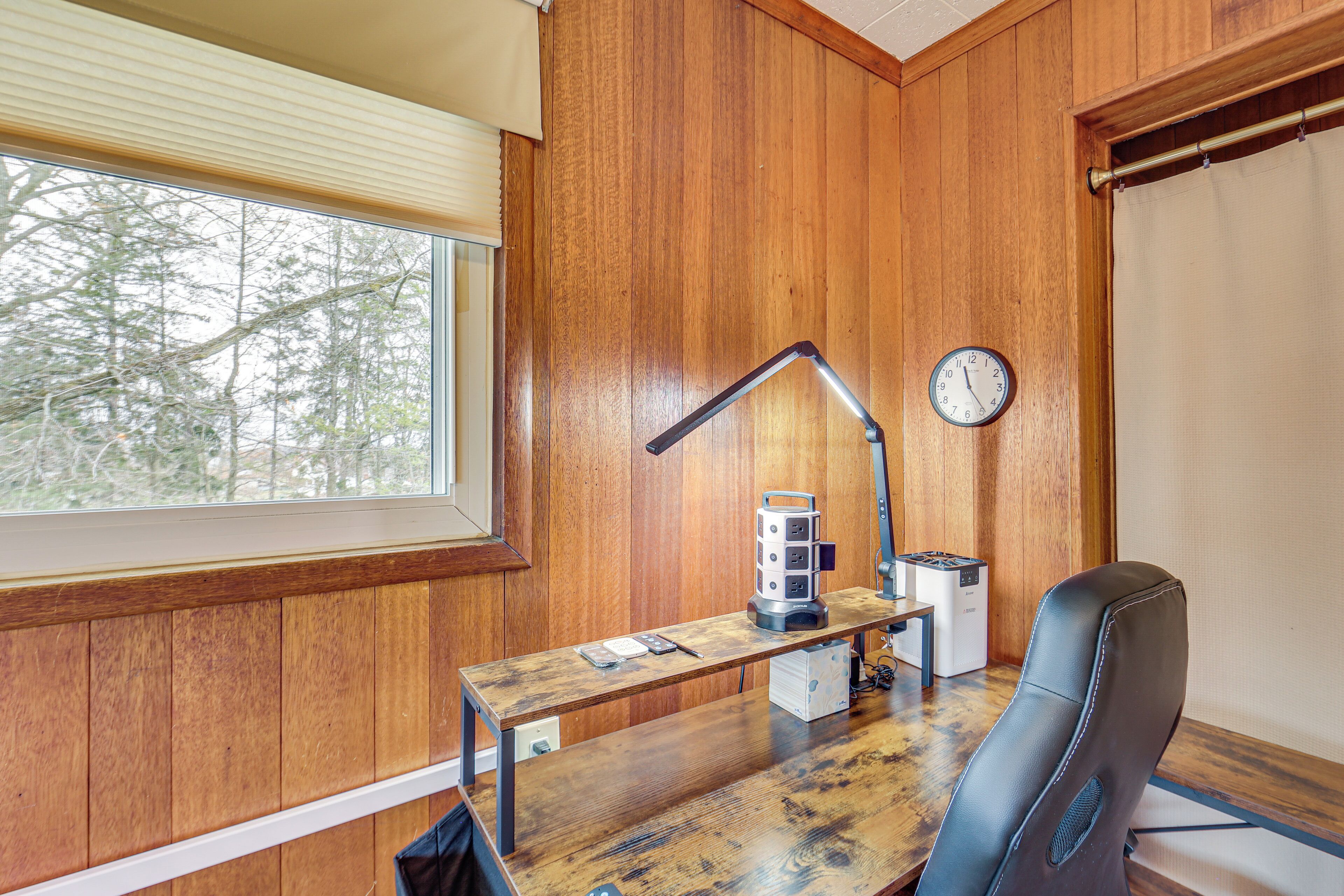 A wooden-paneled room with a desk, a clock, and a window with blinds.
