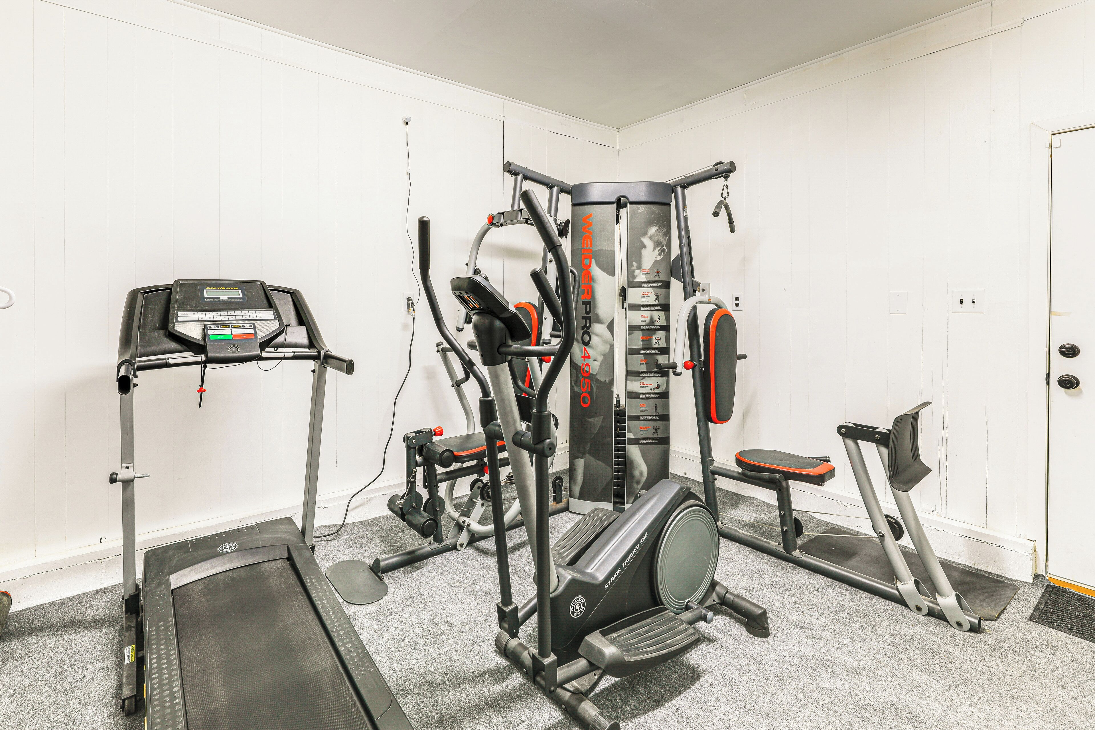 Uma academia com aparelhos de cardio, equipamentos de musculação e um banco.