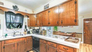 A kitchen with wooden cabinets, a dishwasher, a coffee station, and a dining area with chairs. - 6 Mi to Salisbury: Forest-view Sanctuary! (Parsonsburg)
