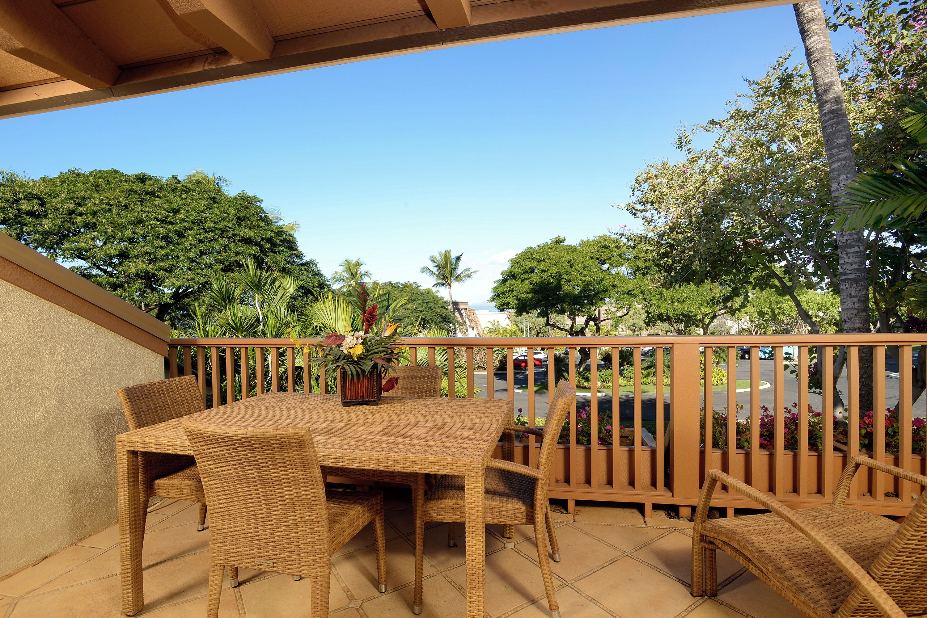 Eine überdachte Terrasse im Freien mit einem Korbstuhl-Garnitur, umgeben von einem Holzzaun und üppiger Bepflanzung.