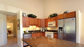 Una cocina con encimeras de granito, gabinetes de madera y electrodomésticos de acero inoxidable, incluyendo un microondas.