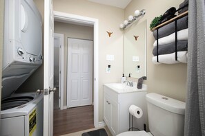 Ein kleines Badezimmer mit Waschmaschine, Toilette, Waschbecken, Handtuch und dekorativer Wandbeleuchtung.