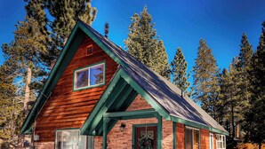 A wooden cabin with a stone foundation, a green roof, and a bear sculpture at the entrance. - Charming Cherokee Cabin Secluded Stay for 6 Just 10 Minutes to Tahoe! (South Lake Tahoe)