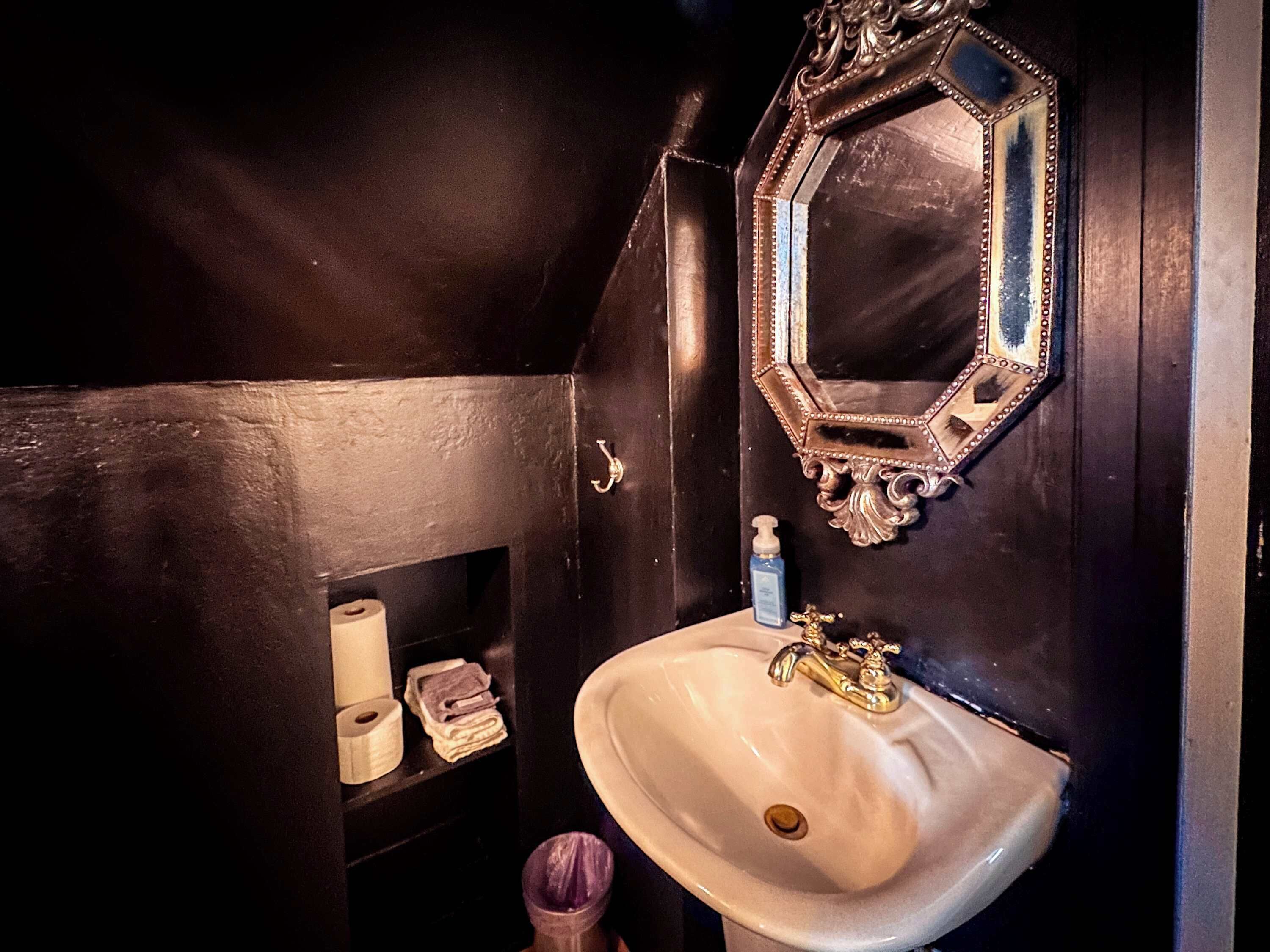 Ein Badezimmer mit einem weißen Waschbecken, einem Spiegel mit aufwendiger Rahmung und einem Ablagebereich für Toilettenartikel.