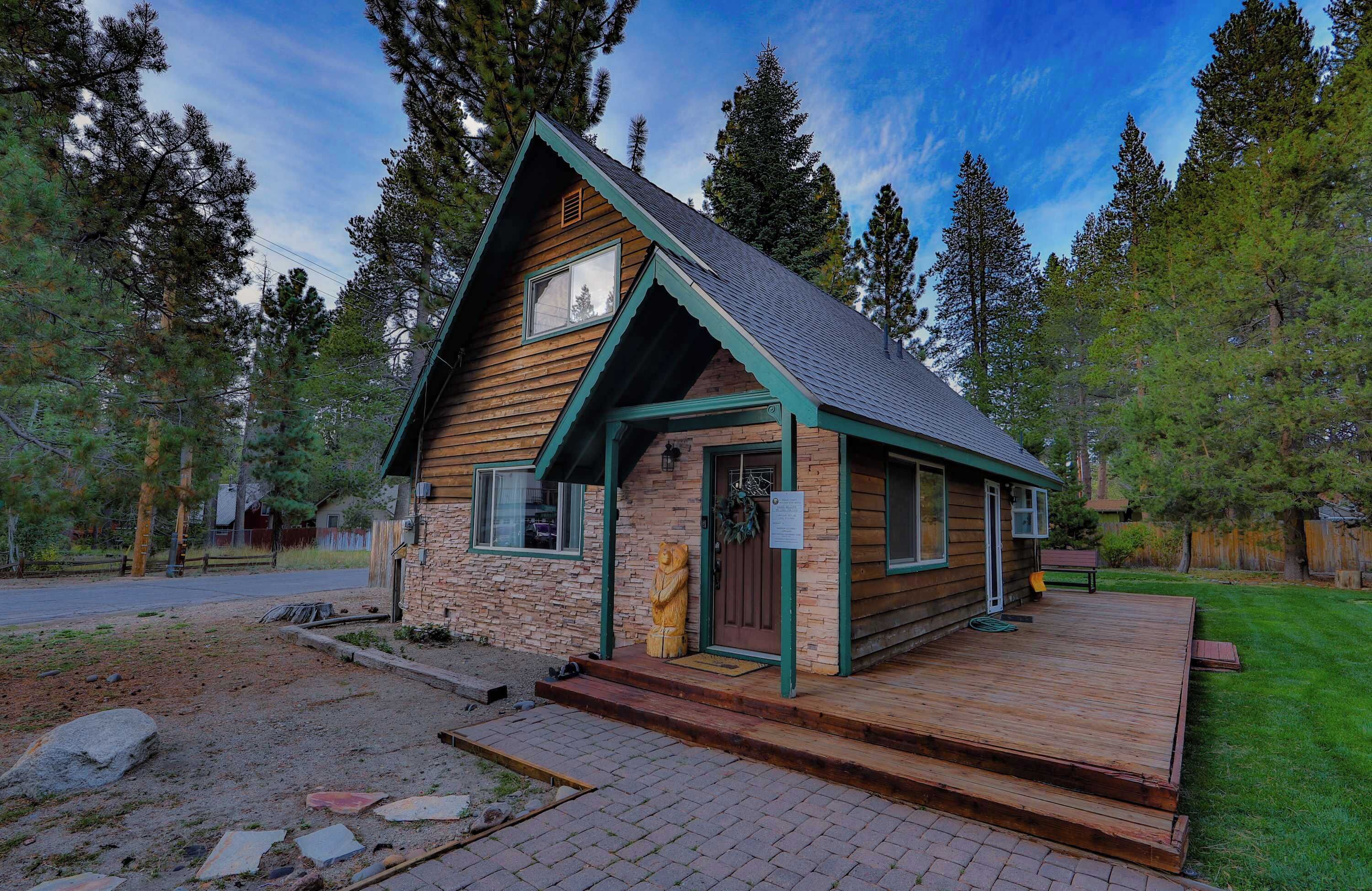 Une cabane en rondins dotée d’une terrasse en bois, de fondations en pierre et d’un toit végétalisé.