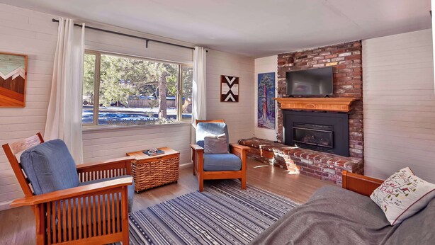 A living room with a fireplace, a TV mounted above it, and a large window with curtains. - Charming Cherokee Cabin Secluded Stay for 6 Just 10 Minutes to Tahoe! (South Lake Tahoe)