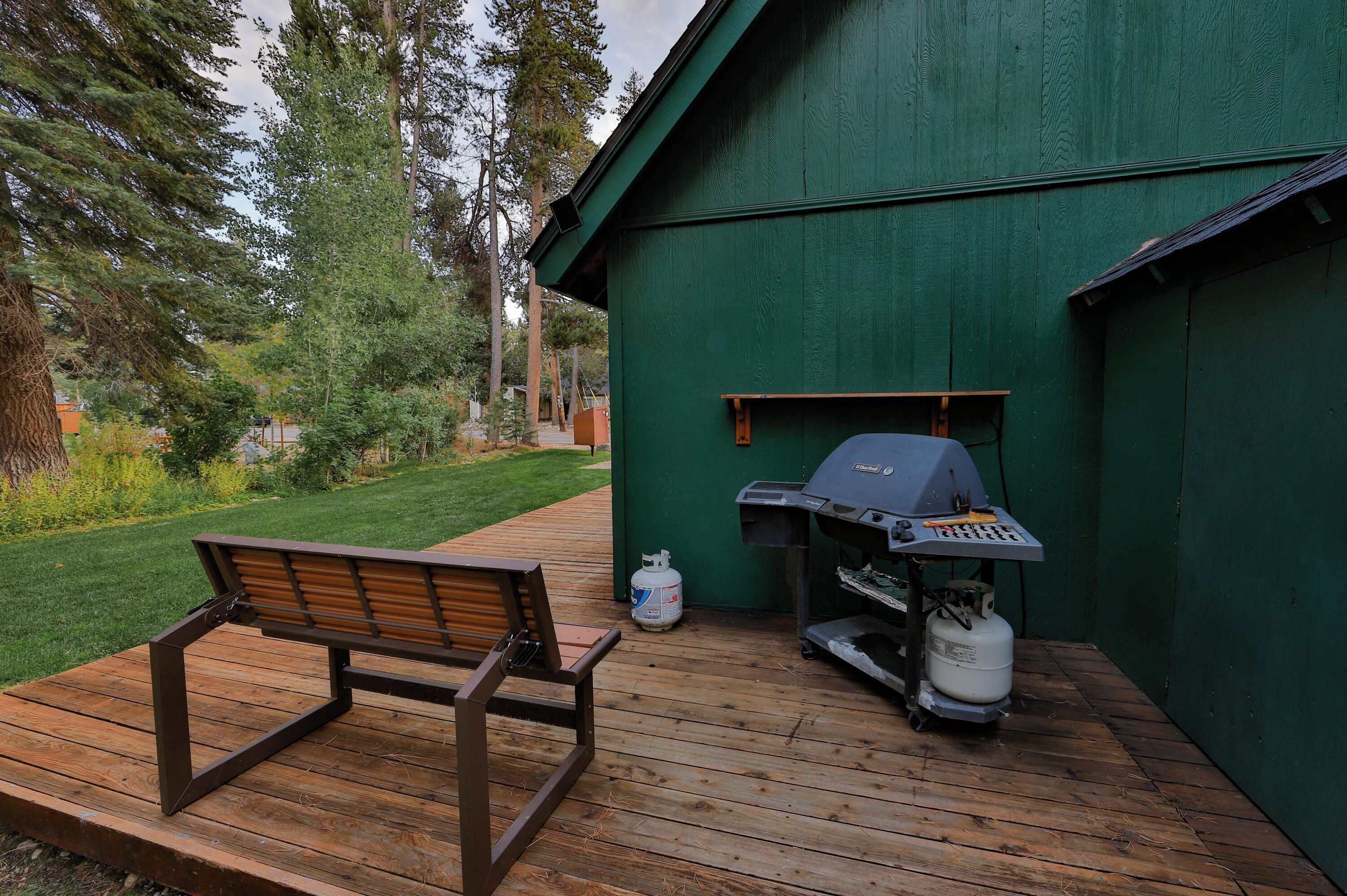 Eine Holzterrasse mit einer Bank, einem Grill und Propangasflaschen.