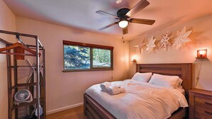 A bedroom with a bed, a ceiling fan, a window with a view, a wall-mounted light, and a wooden nightstand. - Charming Cherokee Cabin Secluded Stay for 6 Just 10 Minutes to Tahoe! (South Lake Tahoe)