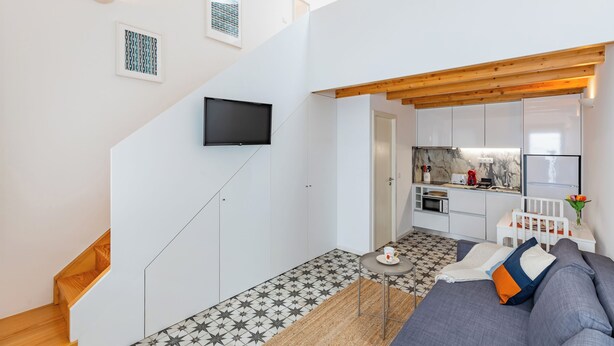 Eine moderne Wohnung mit Treppe, einem Wohnzimmer mit Sofa, einer Küchenzeile und einem an der Wand befestigten Fernseher.