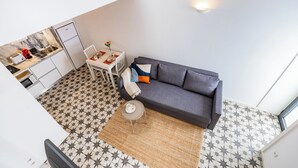 Ein kompakter Wohnbereich mit Küchenzeile, einem grauen Sofa, einem kleinen runden Tisch und einem Fußboden mit Muster.
