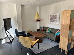 Ein modernes Wohnzimmer mit einer Couch, einem Couchtisch, einem gelben Sessel, einer Stehlampe und einem Bücherregal.