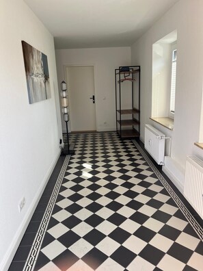 Ein Flur mit Schachbrettfußboden, einem Heizkörper, einer Tür und einem an der Wand befestigten Regal.