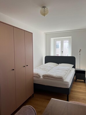 A bedroom with a bed, wardrobe, bedside table, and a window.